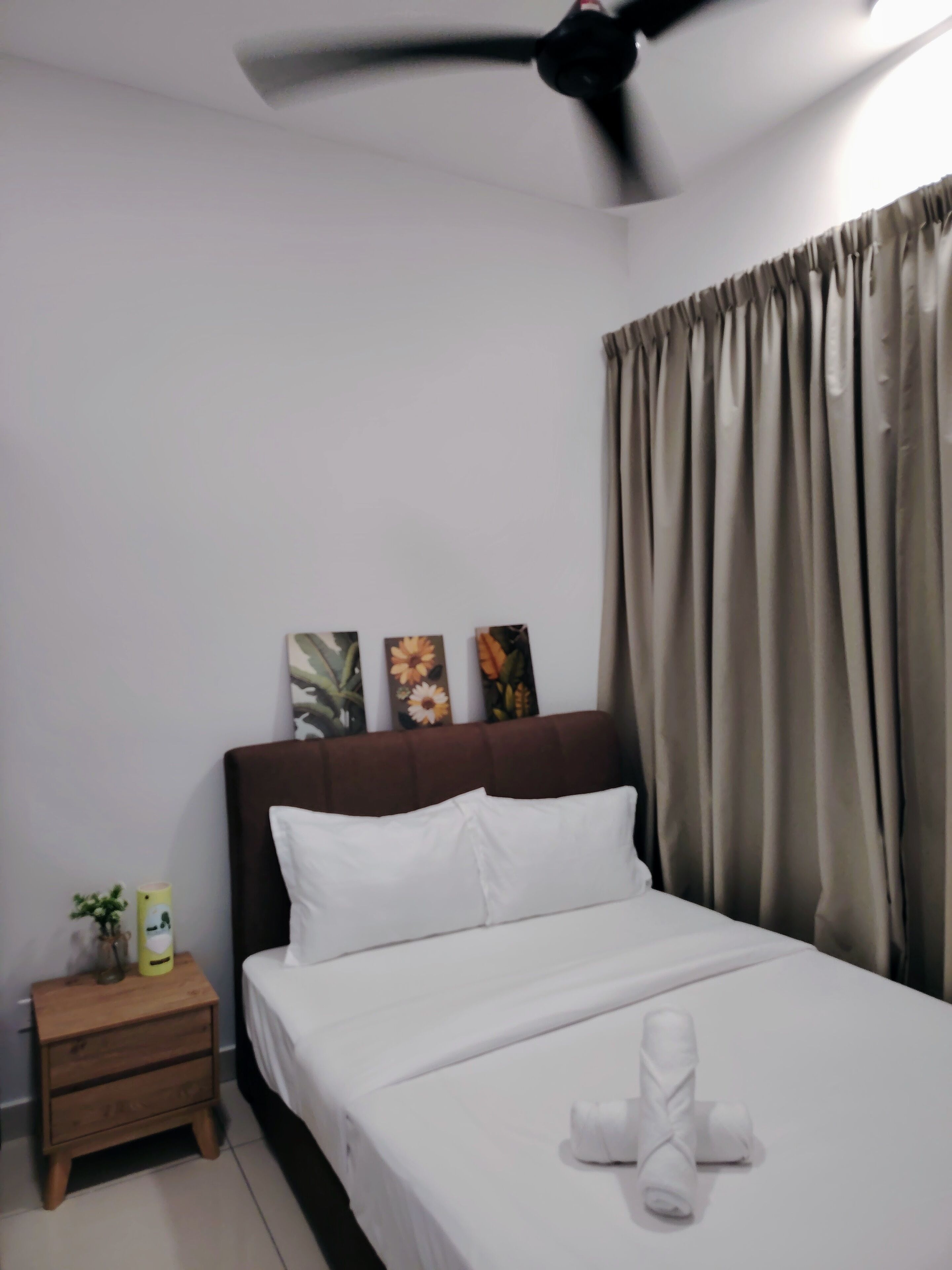 A hotel room with a bed, a nightstand, a ceiling fan, and curtains.