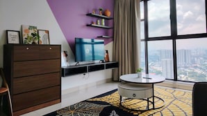 A modern living room with a large window, a flat-screen TV, a wooden cabinet, and a patterned rug. - Trion KL Residence by Sleepy Owl Suites (Kuala Lumpur)