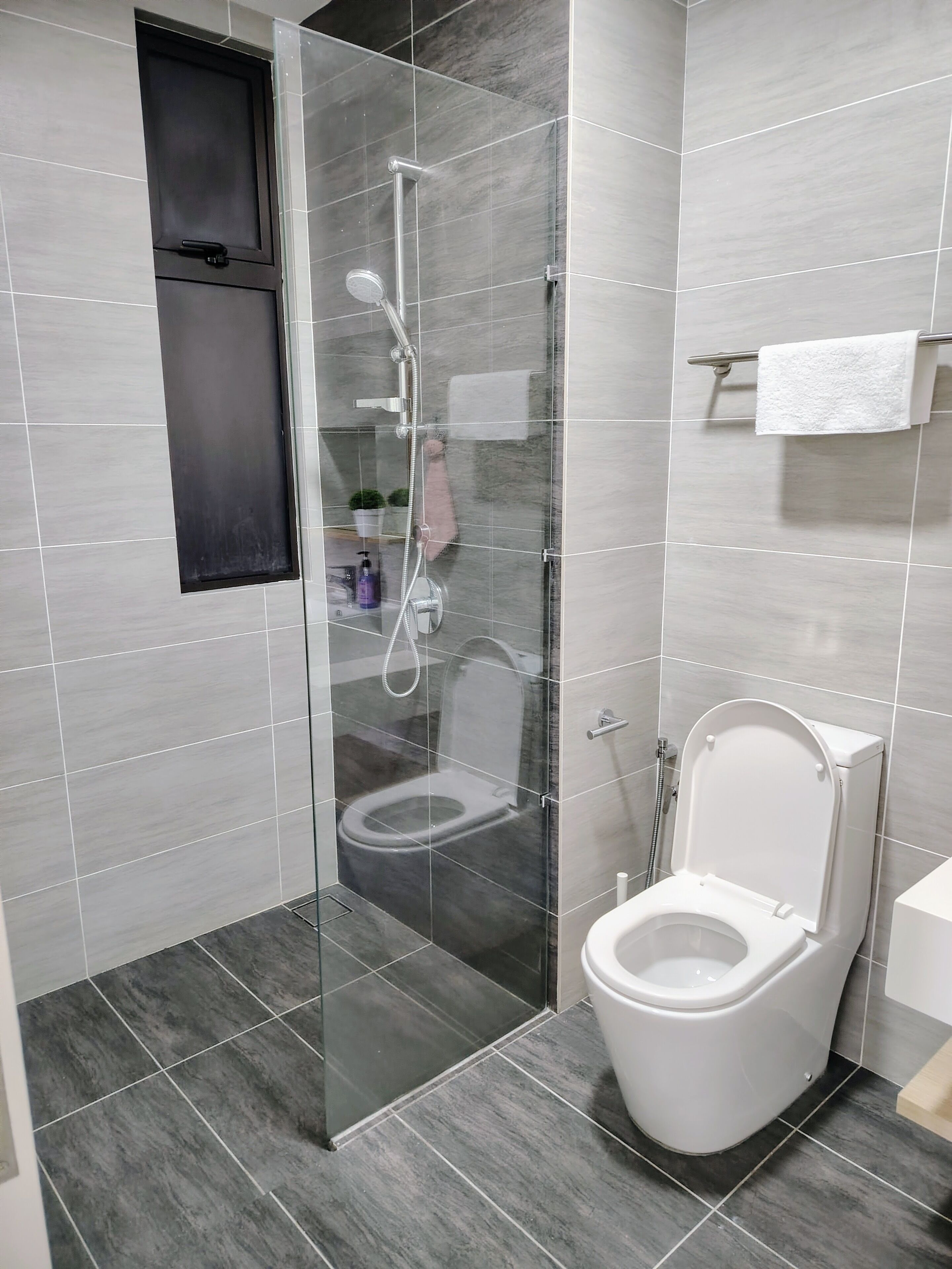 A modern bathroom with a glass-enclosed shower, a toilet, and a towel rack.