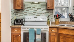 A kitchen with wooden cabinets, a white stove, a toaster, and a window with a view of trees. - Beautiful Get-a-way in the Heart of Sioux Falls (Sioux Falls)