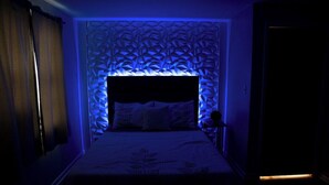 A bedroom with a bed, a headboard with a geometric pattern, and a wall-mounted light fixture. - Beautiful Get-a-way in the Heart of Sioux Falls (Sioux Falls)