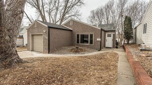 A two-story house with a garage, a small attached shed, and a landscaped yard with a tree and a fire pit. - Beautiful Get-a-way in the Heart of Sioux Falls (Sioux Falls)