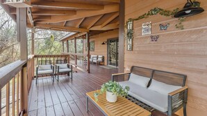 A wooden deck with a sofa and chairs, a table with a plant, and a hanging birdhouse. - A&M Cabin-Pool Table Deck BBQ-10mins Kyle Field (Bryan)
