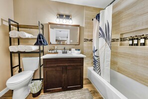 A modern bathroom with a wooden vanity, a toilet, a shower with a curtain, and a towel rack with towels. - A&M Cabin-Pool Table Deck BBQ-10mins Kyle Field (Bryan)