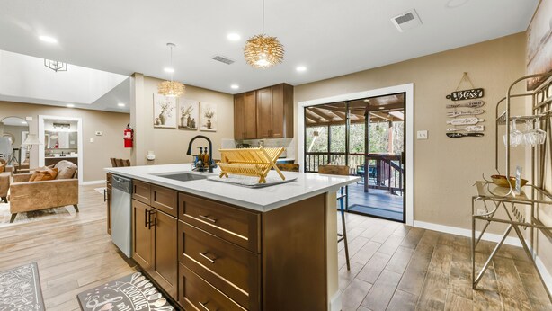 A modern kitchen with a large island, wooden cabinets, and pendant lighting. - A&M Cabin-Pool Table Deck BBQ-10mins Kyle Field (Bryan)