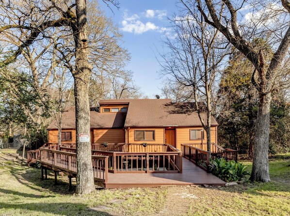 A two-story wooden cabin with a deck and a security warning sign. - A&M Cabin-Pool Table Deck BBQ-10mins Kyle Field (Bryan)