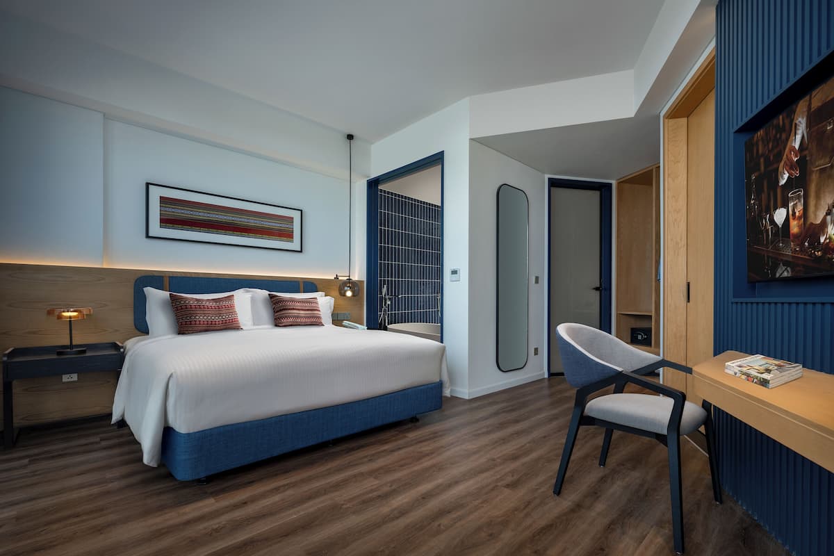 A modern hotel room with a large bed, a desk, and a mirror.