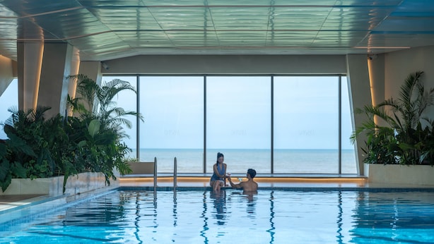 A swimming pool with a view of the ocean, surrounded by indoor plants and a glass ceiling. - Lasong Hotel & Villas Sam Son By The Unlimited Collection (Nam Sam Son)