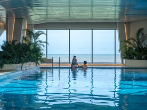 Piscina con vista al océano, rodeada de plantas de interior y un techo de cristal.