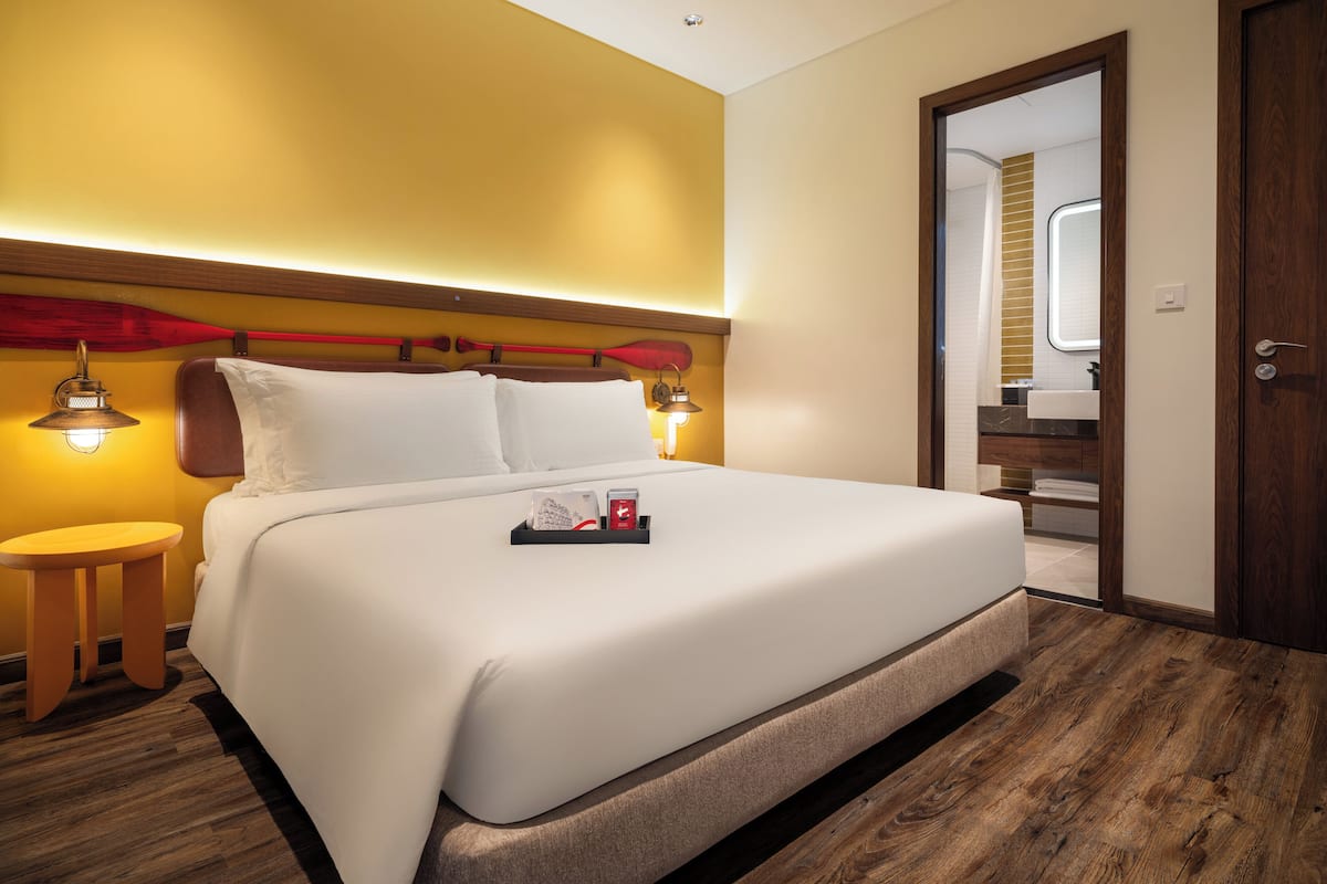 A hotel room with a large bed, wooden headboard, bedside lamps, and a wooden floor.