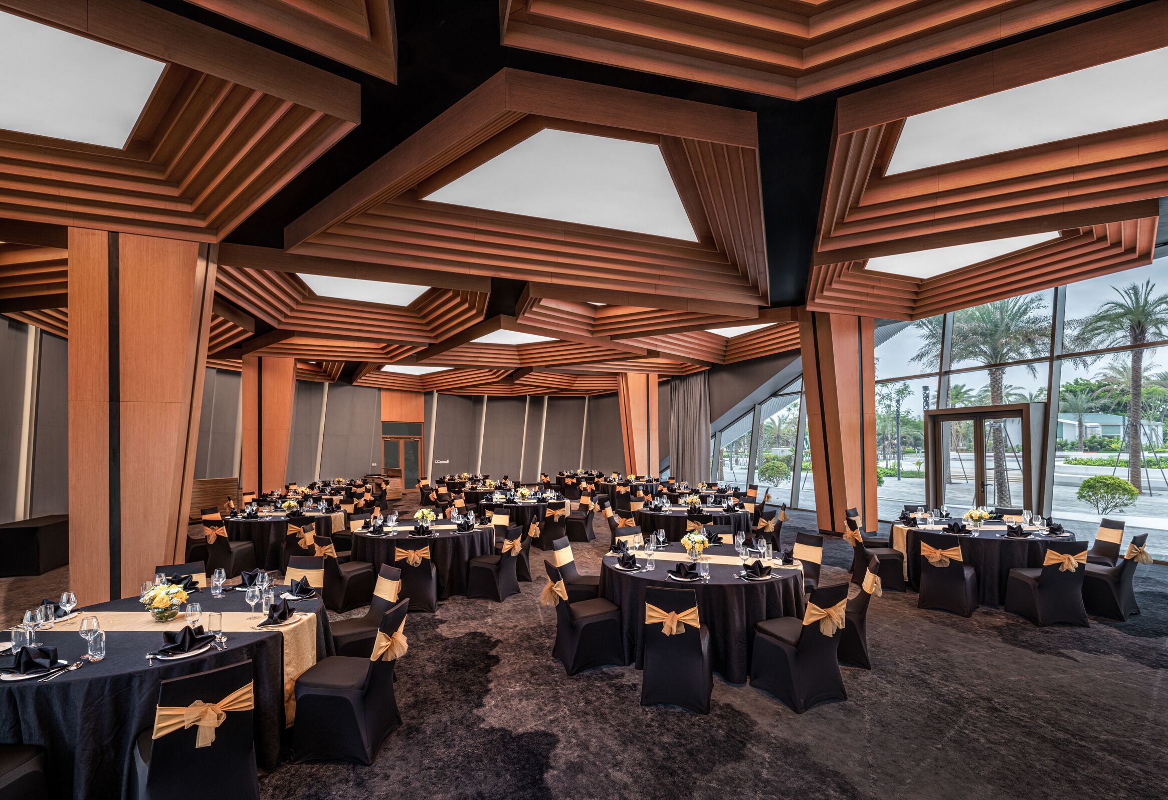 A conference room with multiple tables, black chairs with gold sashes, and a modern ceiling design.