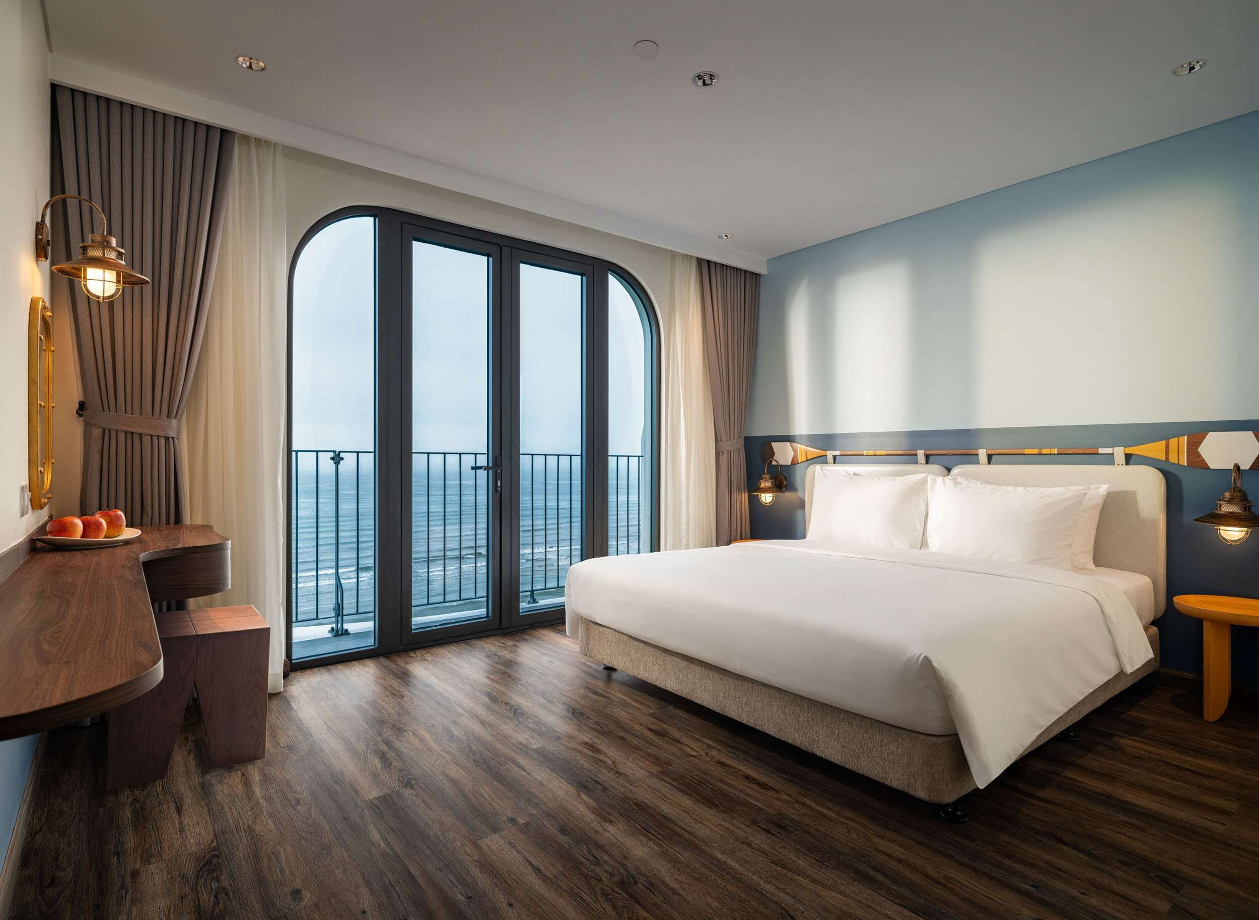 Ein Hotelzimmer mit einem großen Bett, einem Holztisch, einem Stuhl und Meerblick durch eine Glastür.