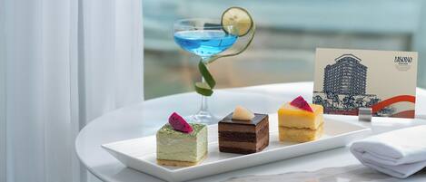 A table with desserts and a cocktail, a folded napkin, and a business card, with a view of the sea in the background.