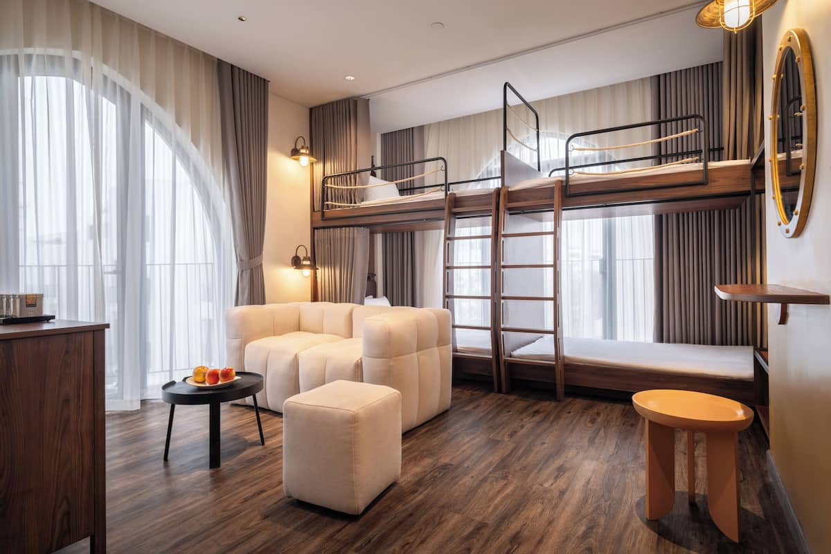 A modern hotel room with a bunk bed, a sofa, a small table with fruit, and a wooden floor.