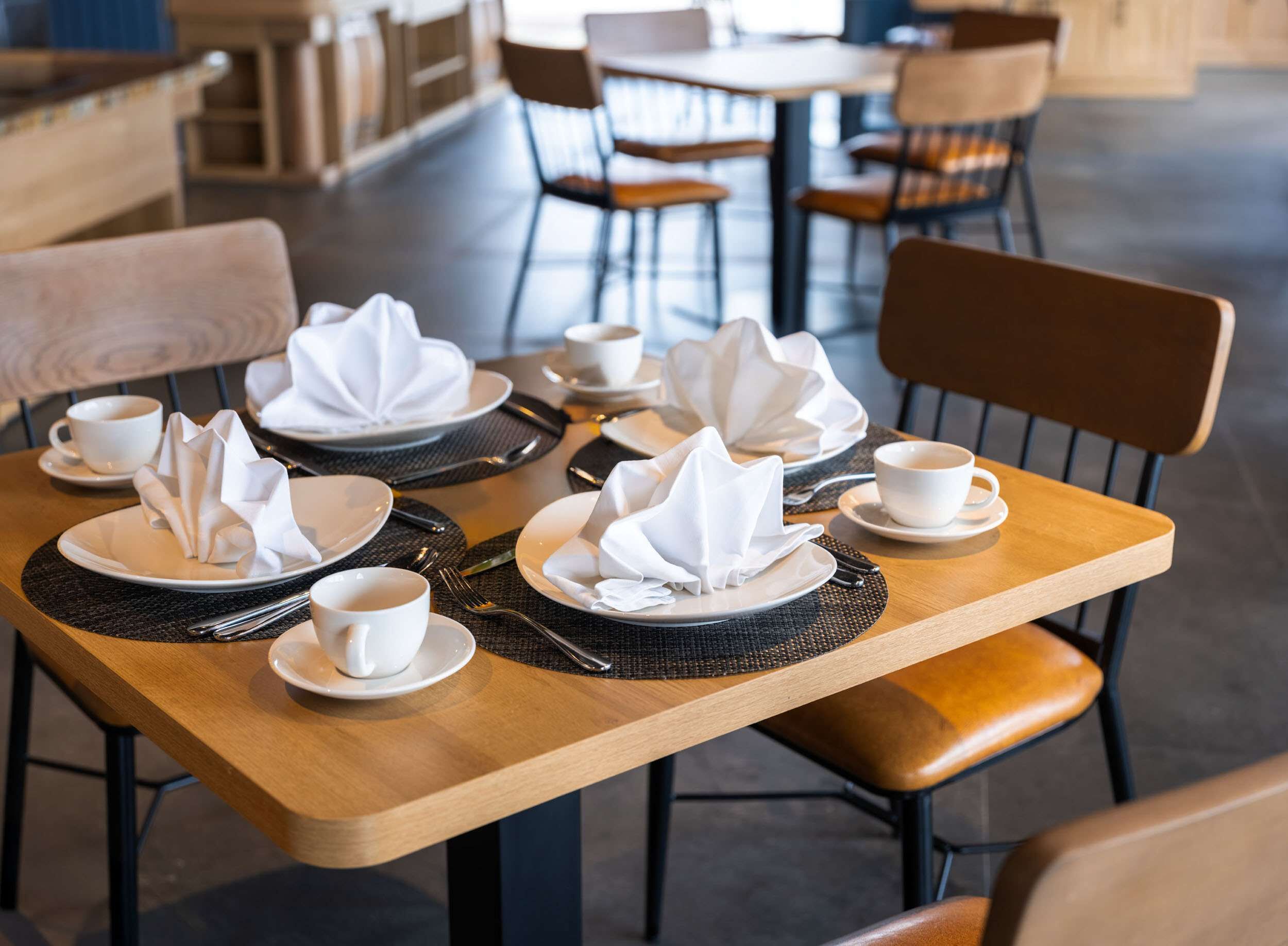 A neatly set dining table with white napkins, plates, and cups, suggesting a clean and organized dining area.