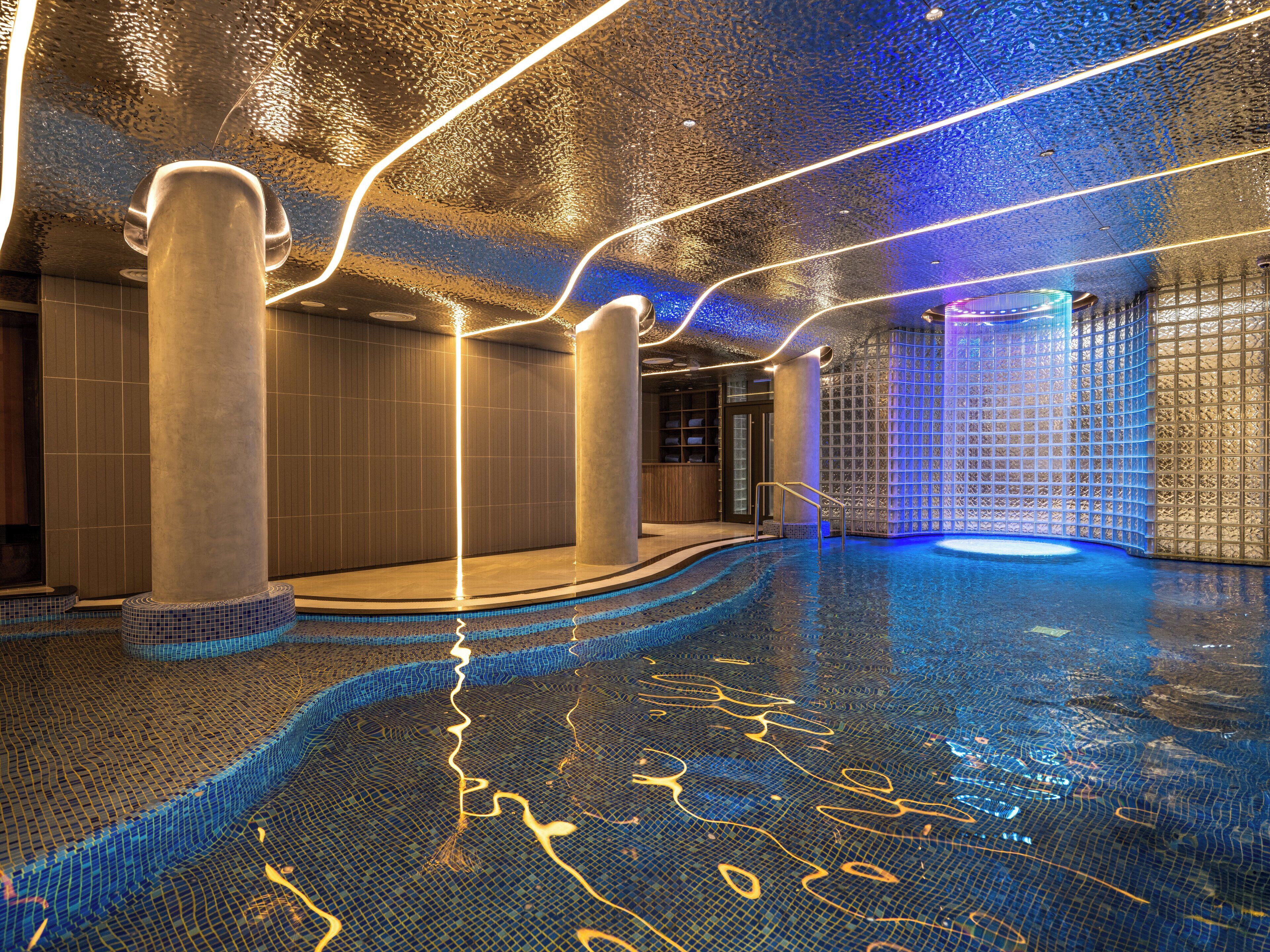 Une piscine intérieure avec un sol carrelé et un plafond éclairé en bleu.