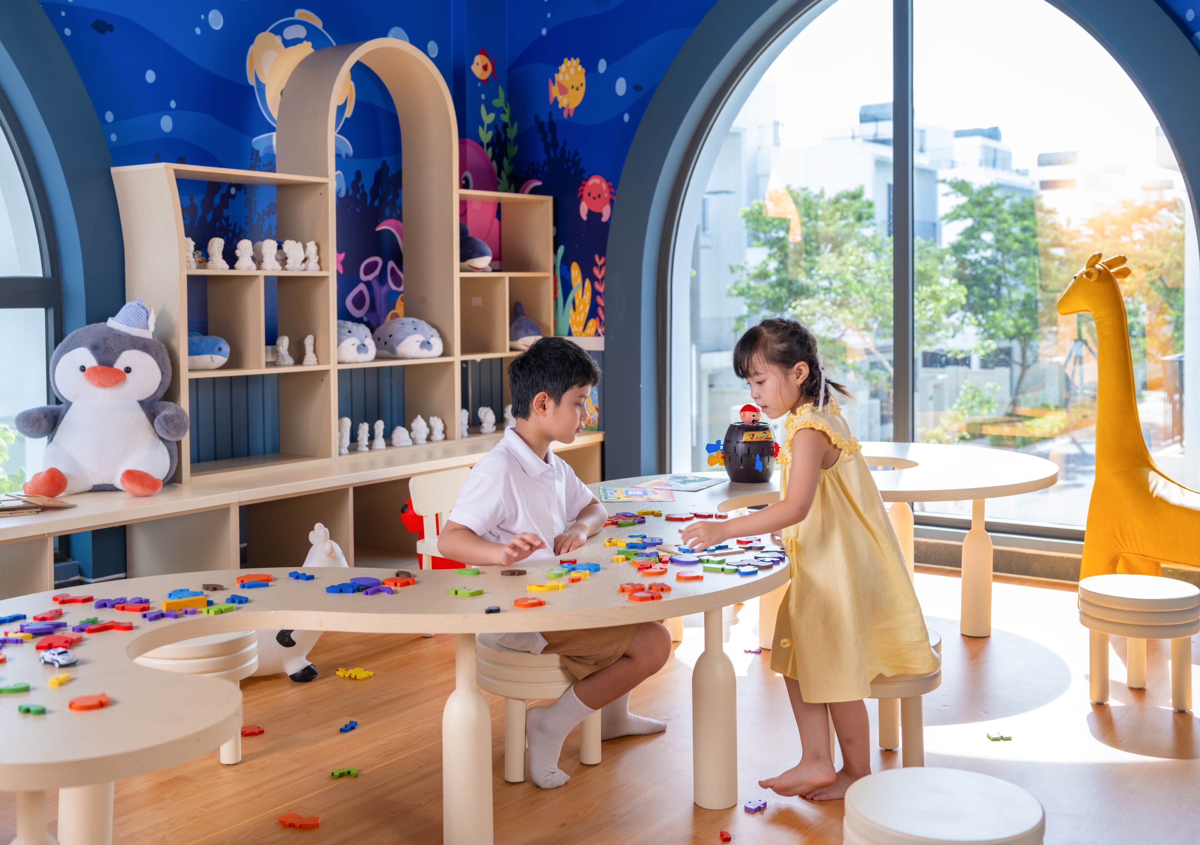 A children's play area with a large table, shelves with toys, and a giraffe decoration.