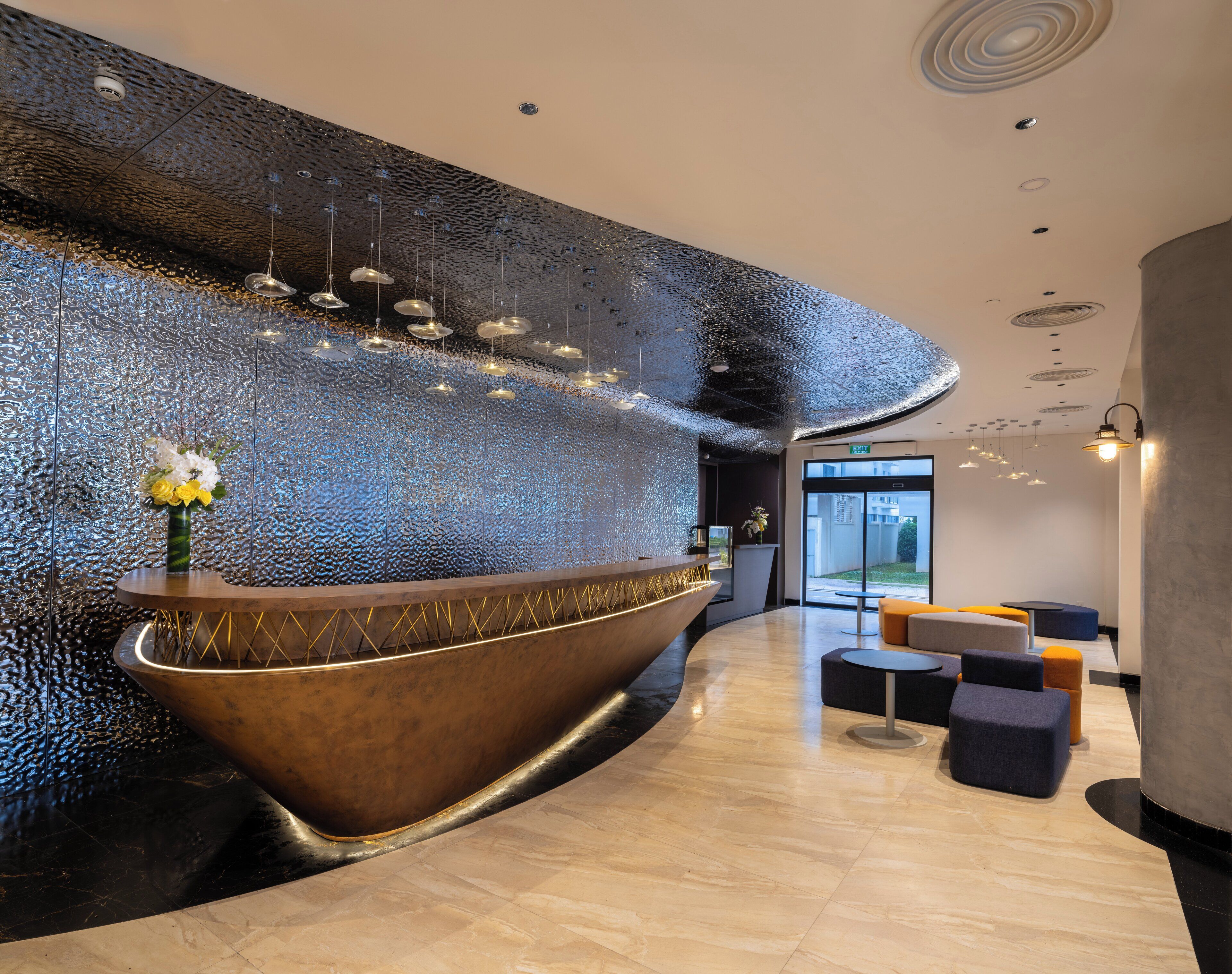 Un espace d’accueil moderne, doté d’un grand comptoir d’accueil aux lignes courbes, d’un mur à texture et d’un éclairage contemporain.