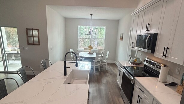 A modern kitchen with a central island, white cabinetry, and a dining area with a chandelier. - 1 Acre Rolling Hills Home (Ocala)