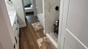 A hallway with wooden flooring, white walls, and a marble backsplash. There are two rugs on the floor and a small table with a bottle on it. - 1 Acre Rolling Hills Home (Ocala)
