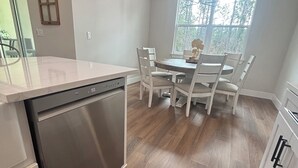 A kitchen with a dishwasher, a dining table with chairs, and a window with a view of trees. - 1 Acre Rolling Hills Home (Ocala)