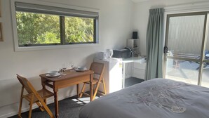 A hotel room with a bed, a dining table with chairs, a microwave, a small cabinet, and a window with a view of greenery. - Country Getaway - Studio room with Ensuite in seven-acre landscaped gardens. (Waitohi)