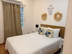 Ein Schlafzimmer mit einem Bett, einem Nachttisch, einer Lampe, einem Fenster mit Vorhängen und zwei Wanddekorationen.