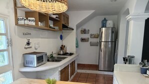 Eine kompakte Küche mit Mikrowelle, Kaffeemaschine und Kühlschrank. Ein kleiner Esstisch trägt eine Pflanze.