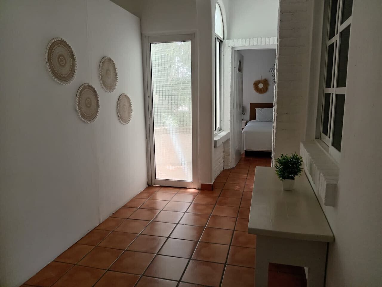 A hallway with tiled flooring, a white wall with decorative plates, a door leading to another room, and a small table with a plant.