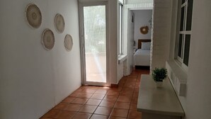 Ein Flur mit Fliesenboden, eine weiße Wand mit dekorativen Platten, eine Tür zu einem anderen Raum und ein kleiner Tisch mit einer Pflanze.