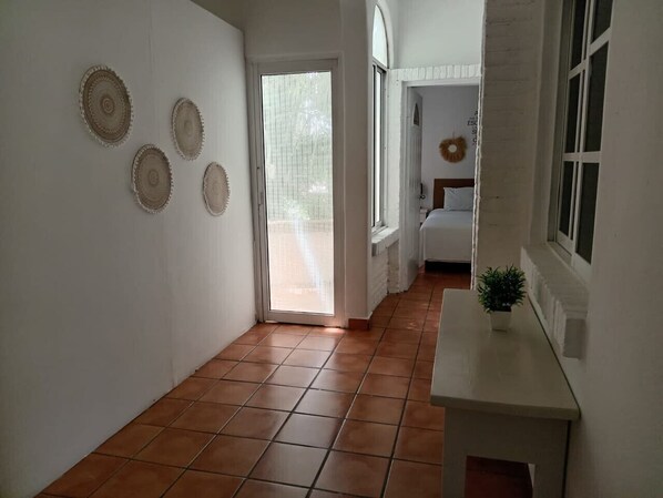 A hallway with tiled flooring, a white wall with decorative plates, a door leading to another room, and a small table with a plant.