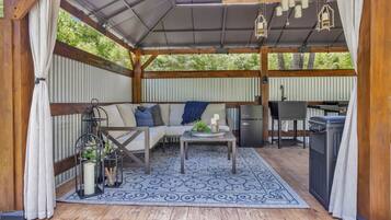 A covered outdoor seating area with a sofa, table, and grill.