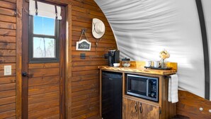 Una cocina compacta con armarios de madera, microondas, cafetera y un lavamanos pequeño.