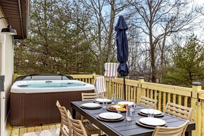 Eine Holzterrasse mit Whirlpool, Esstisch für vier Personen und Stühlen.