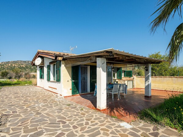 A small house with a tiled patio, a covered outdoor seating area, and a view of the countryside.
