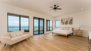 A bedroom with a bed, a sofa, a ceiling fan, and large windows with a view of the sea. - NEW Luxury 4,000 SF Waterfront Home, With Pool, Sleeps 20 (Port Isabel)