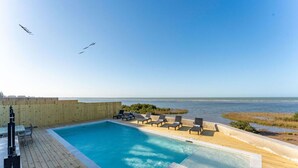 A pool with lounge chairs, a wooden deck, and a view of the ocean. - NEW Luxury 4,000 SF Waterfront Home, With Pool, Sleeps 20 (Port Isabel)