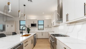 A modern kitchen with white cabinetry, a central island with a sink, a stove, and overhead lighting. - NEW Luxury 4,000 SF Waterfront Home, With Pool, Sleeps 20 (Port Isabel)