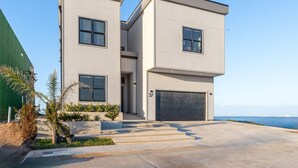 A modern two-story house with a garage, a driveway, and a view of the ocean. - NEW Luxury 4,000 SF Waterfront Home, With Pool, Sleeps 20 (Port Isabel)