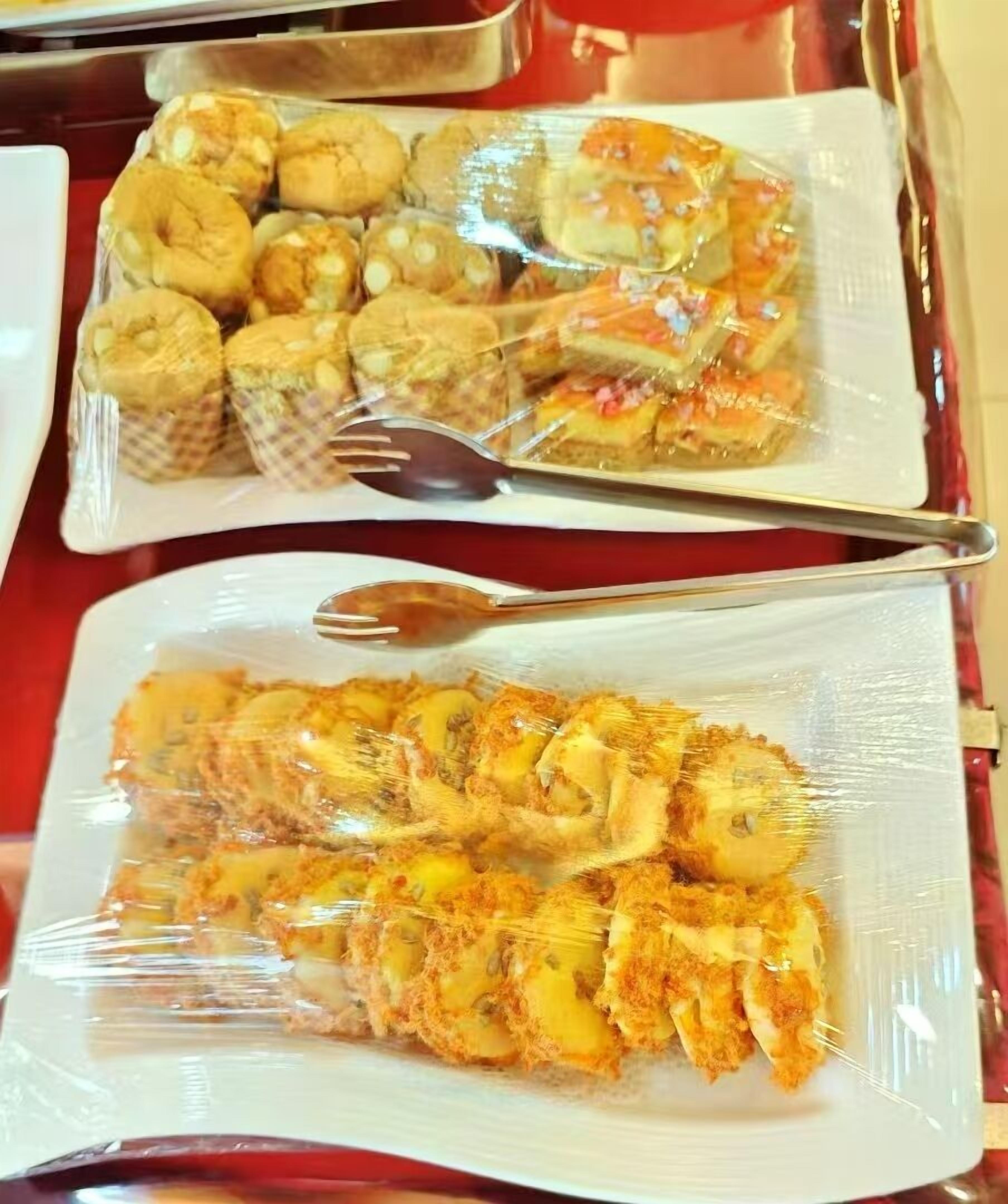 Two trays of food items wrapped in plastic, one containing pastries and the other containing breaded and fried items.