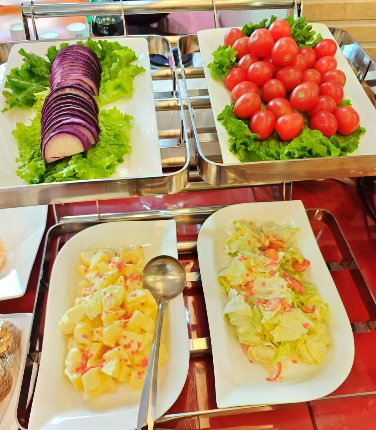 A buffet table with various dishes including sliced red onions, cherry tomatoes, pineapple chunks, and a salad with lettuce and shrimp.