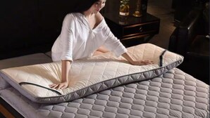 Eine Person richtet eine Matratze auf einem Bett zurecht.