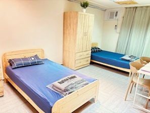 Quarto com duas camas de madeira, um guarda-roupa de madeira, uma mesa pequena e uma cadeira.