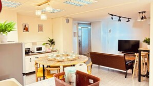 Eine moderne Küche mit Mikrowelle, Toaster und Kühlschrank. Es gibt einen Essbereich mit einem runden Tisch und Stühlen sowie einen Fernseher auf einem Schrank.