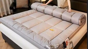 Ein Bett mit grauem Matratze und einem schwarzen Kopfteil.