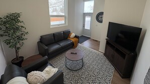 A living room with a black leather sofa, a coffee table, a television, and a potted plant. - Family-friendly remodelled historical church to private suits!
10 min to Costco! (Redcliff)