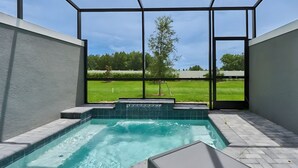 Una bañera de hidromasaje moderna al aire libre, con vista despejada a un césped verde y árboles a través de amplias ventanas.