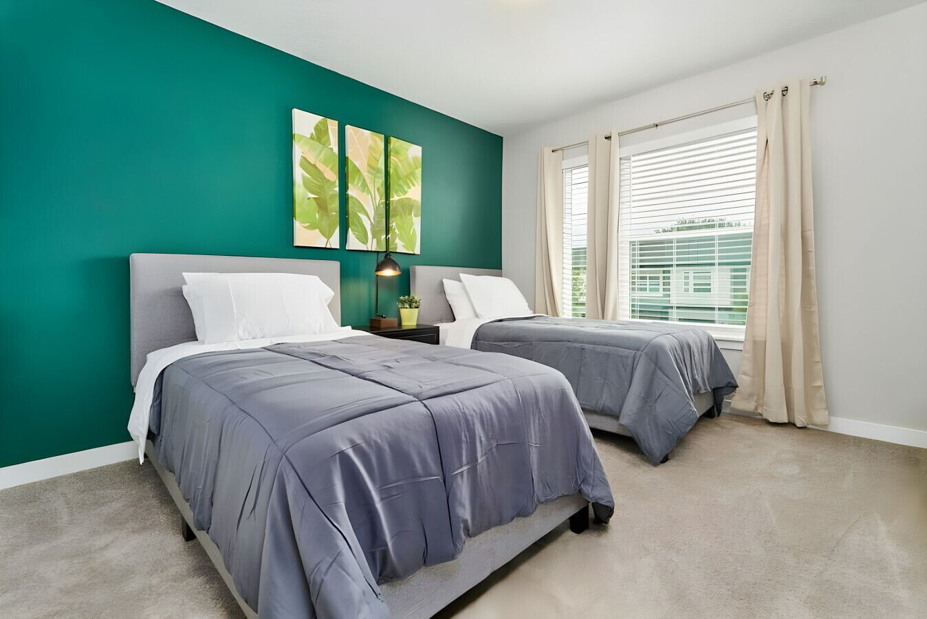 A bedroom with two beds, teal walls, and a window with blinds.