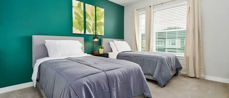 A bedroom with two beds, teal walls, and a window with blinds.
