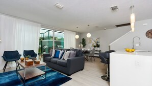 Una sala de estar moderna con un sofá gris, sillas azules y un comedor con una mesa y sillas blancas.